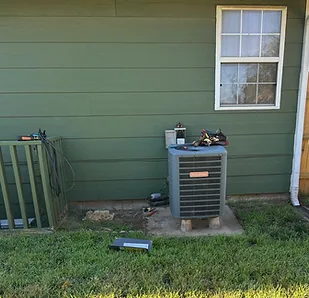 New outdoor condensing unit set on a pad beside a green-sided house